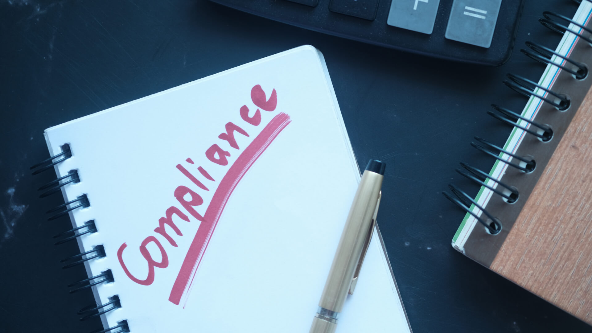 a notepad with the word compliance next to a pen and calculator