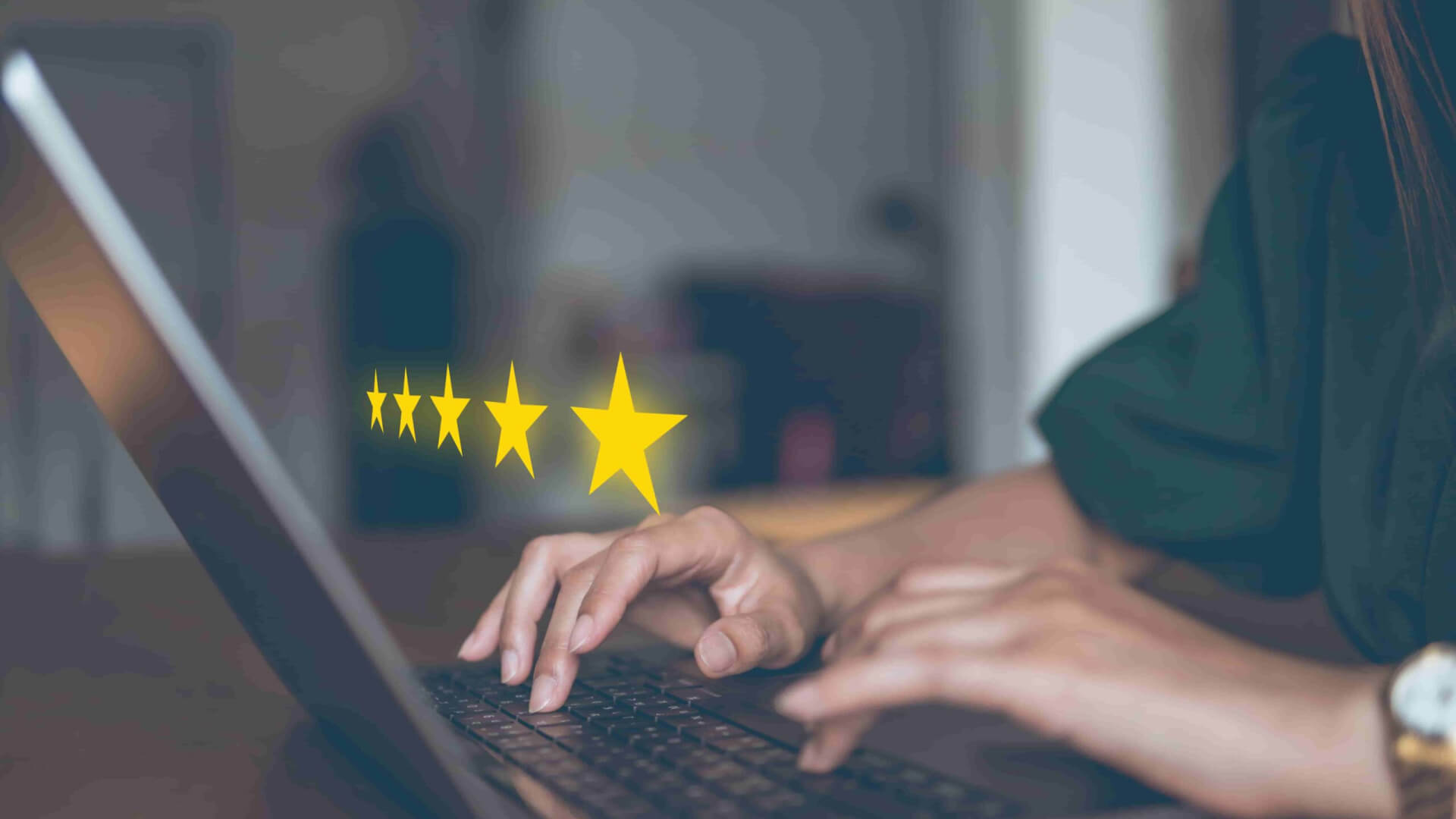 Hands typing on a laptop with four floating yellow stars above, in a dimly lit room.