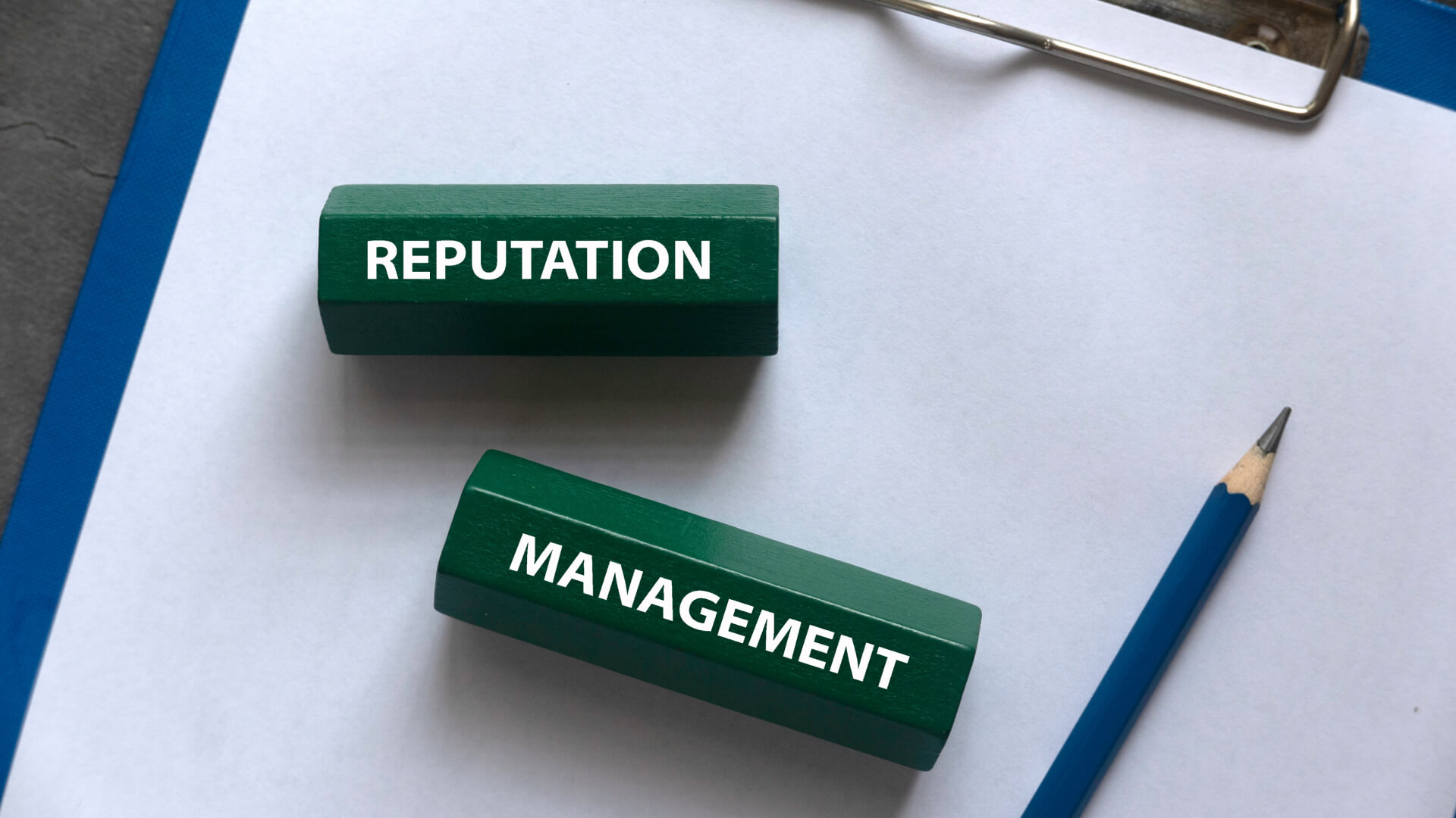 Green blocks with REPUTATION and MANAGEMENT on white paper, beside a blue pencil.