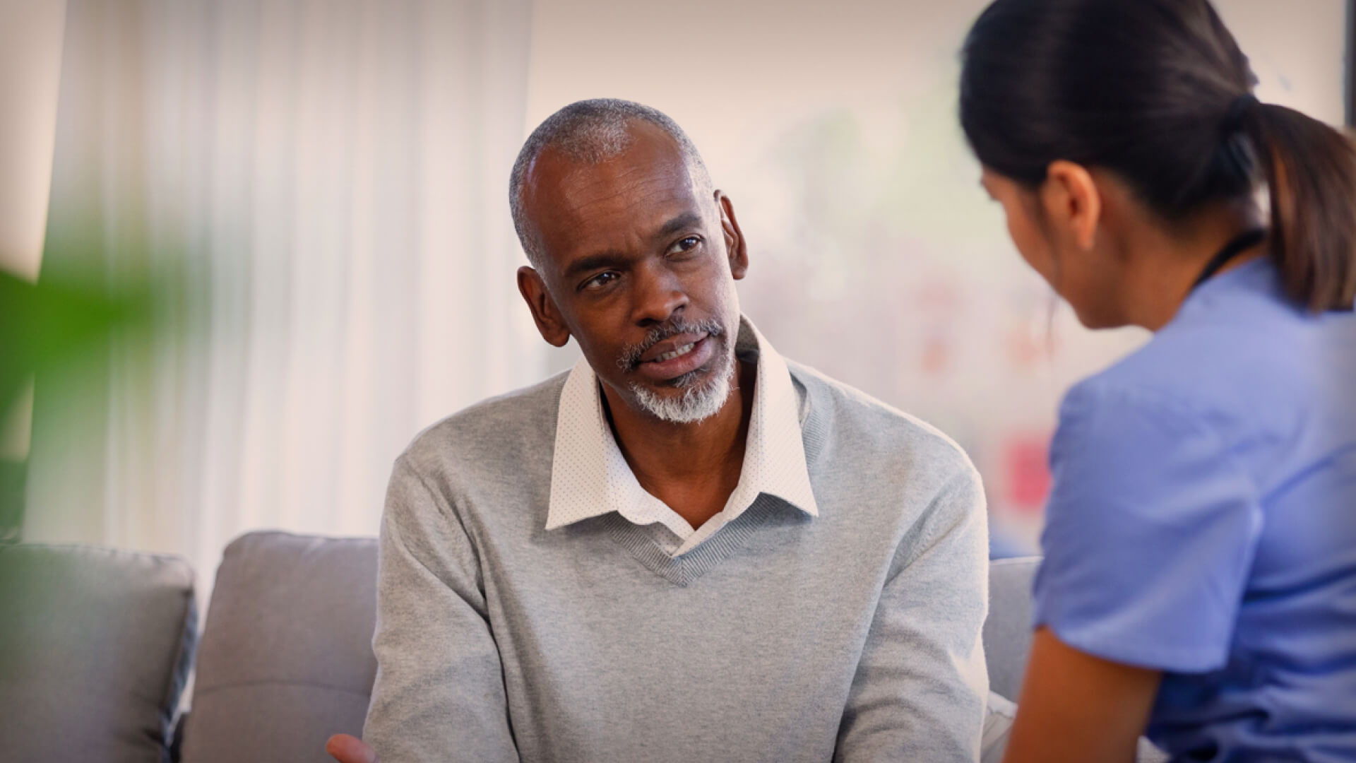 a nurse talking to an older man on a couch