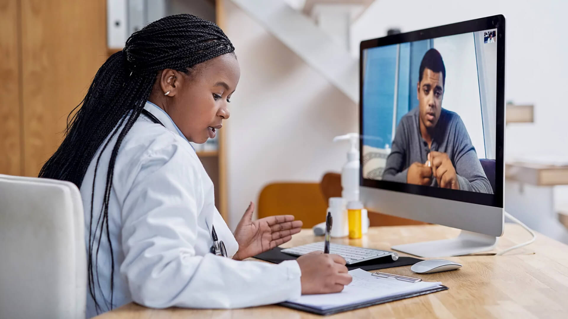 a woman in a white coat is sitting at a desk looking at a computer screen