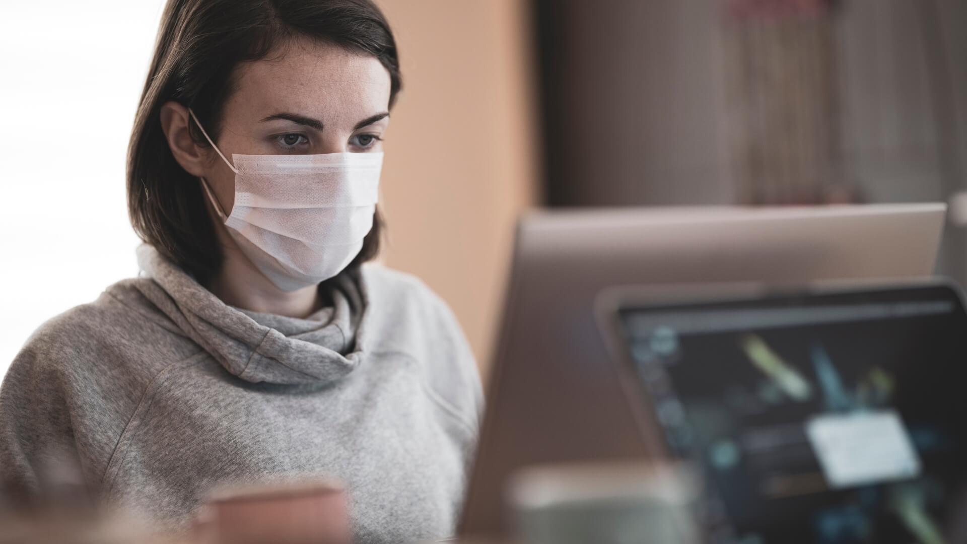 a woman wearing a surgical mask while working on her laptop