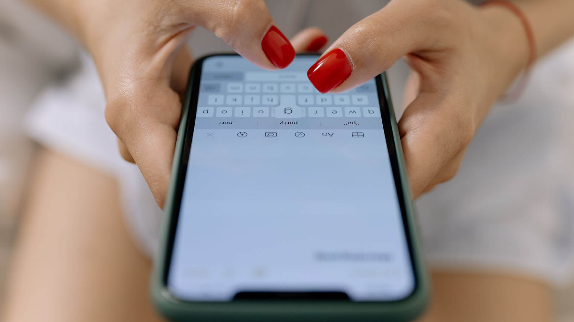 hands of a woman with red nails typing on a smartphone